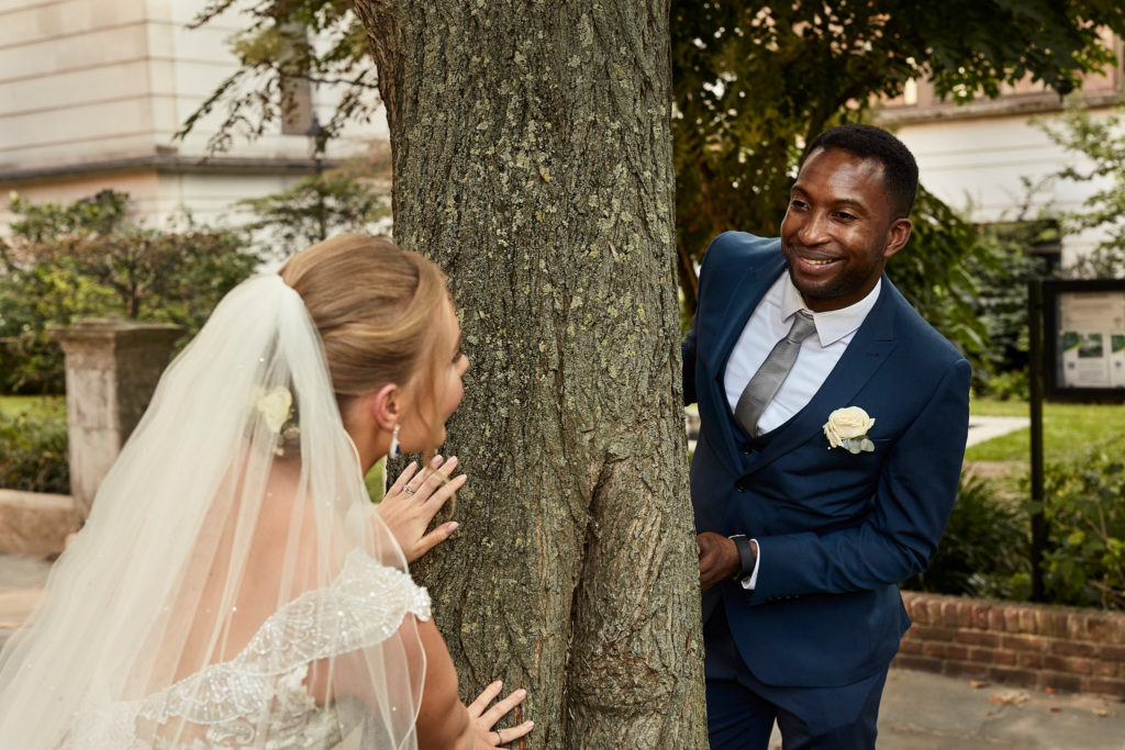 Bride peeking round a tree at the groom